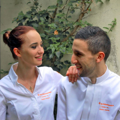 Deux chefs, une femme à gauche et un homme à droite en veste de cuisinier blanche brodée orange