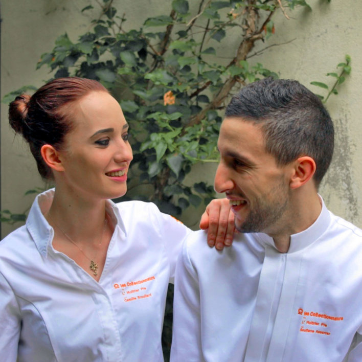 Deux chefs, une femme à gauche et un homme à droite en veste de cuisinier blanche brodée orange