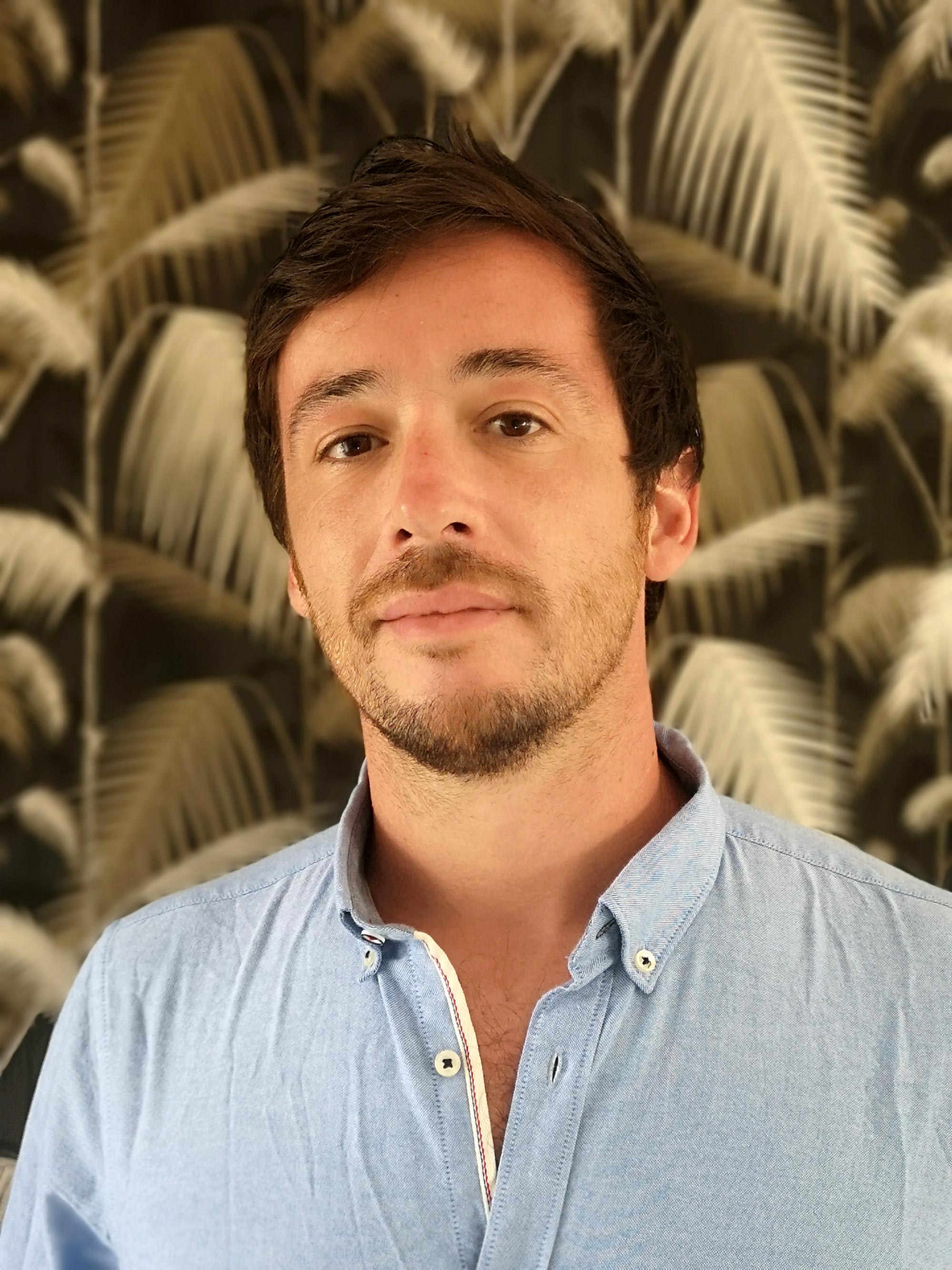 Portrait d'un homme en chemise bleu, arrière plan papier peint noir avec motifs feuilles exotiques dorées