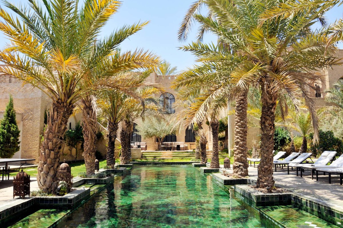 Grande piscine extérieure bordée de palmier au cœur d'un riad tunisien