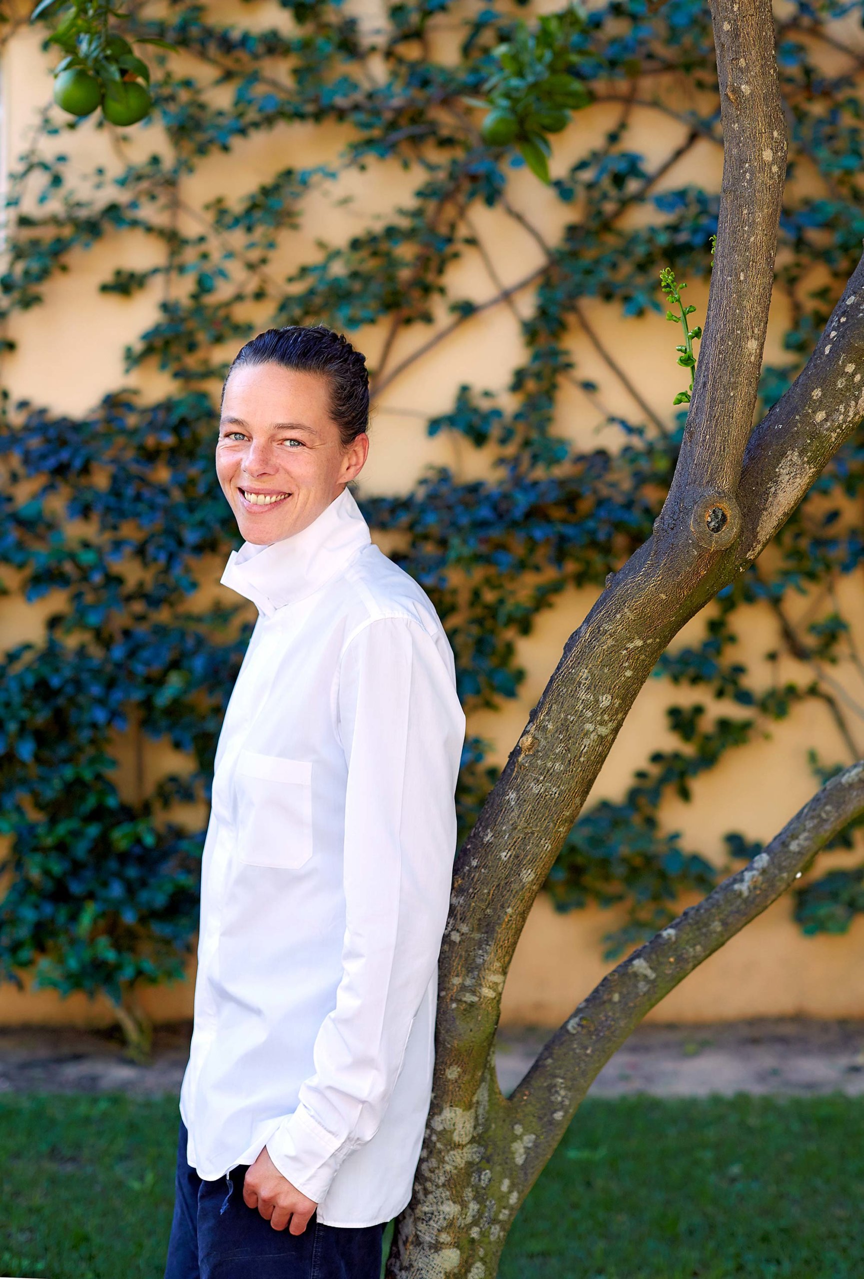 Femme avec chemise blanche, adossée à un arbre dans un jardin