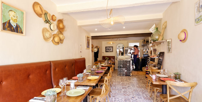 Intérieur d'une salle de bistrot typique provençale avec table et banquette bistrot, chapeau de paille accrochés au mur et toile de Vincent van Gogh