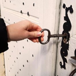 Main tenant une clef noire dans une porte ancienne avec serrure en fer forgé