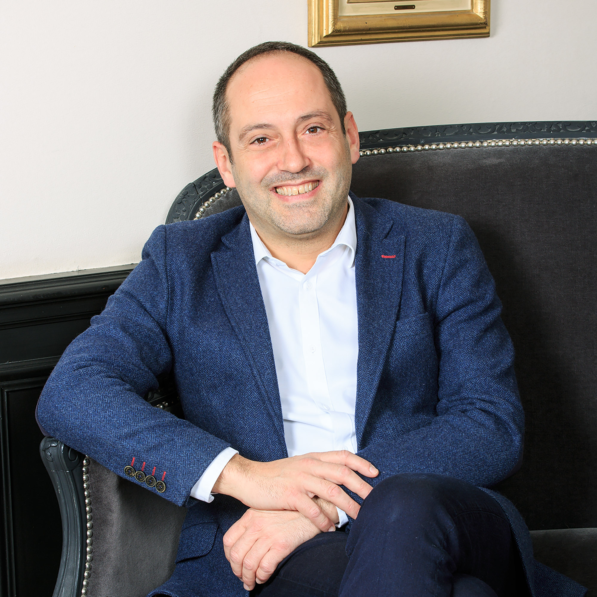Portrait d'un homme en veste de costume bleue, il est assis dans un fauteuil en cuir marron