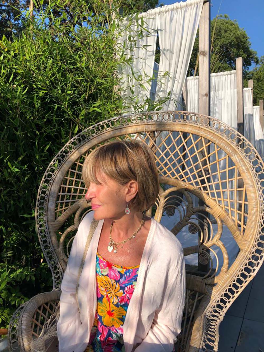 Femme assise dans un fauteuil en rotin sur une terrasse ombragée