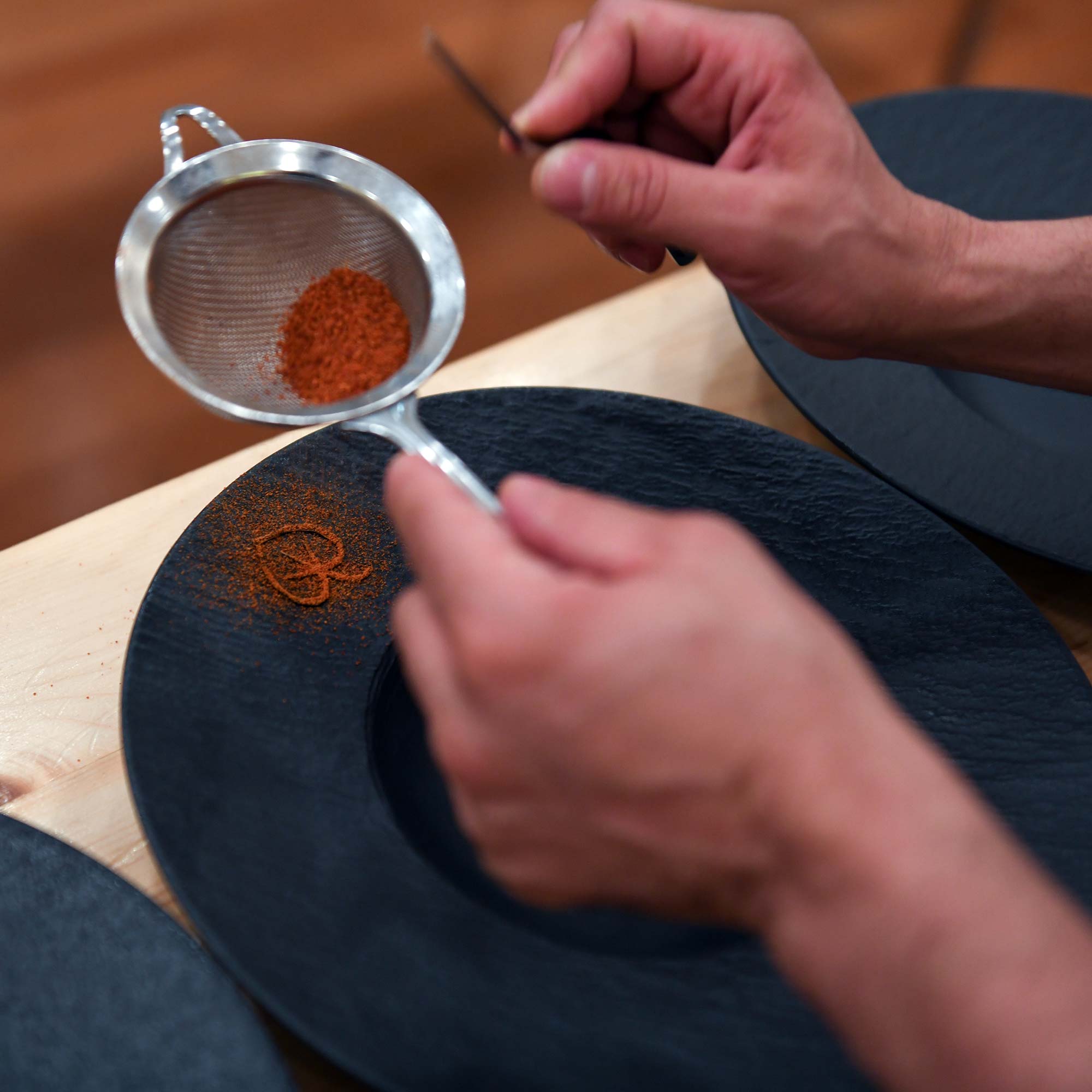 Une main dépose une épices en tamis sur une assiette