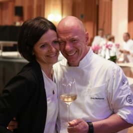 Une femme en blazer noir et un homme en veste de chef, dans les bras l'un de l'autre