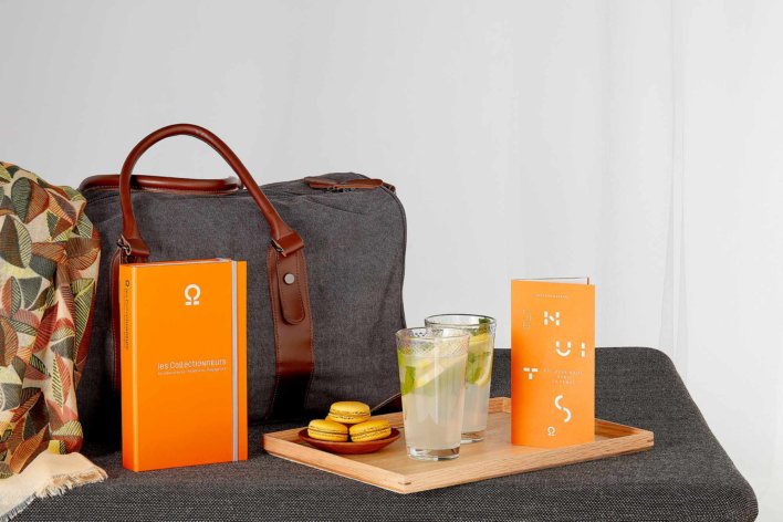 Coffret cadeau poser à coter d'une petite valise grise avec un petit plateau en bois où se trouve deux verres de mojito et une petite assiette de macarons