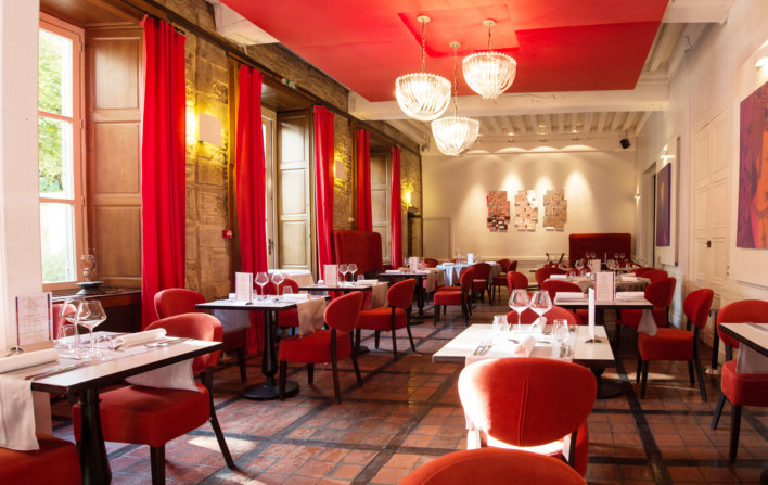 Photo de la salle du restaurant avec des sièges de couleurs rouge et des tables avec des nappes de couleurs blanche