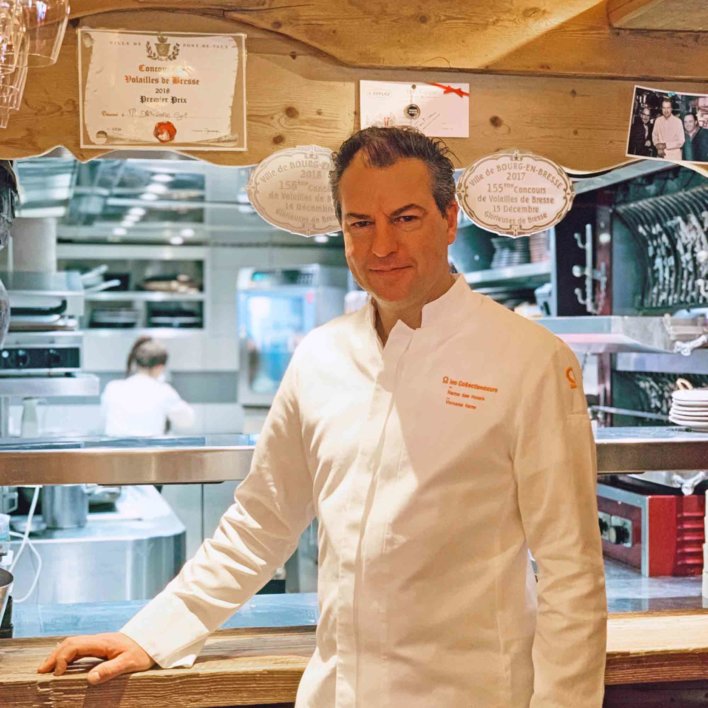 Photo portrait d'un chef en veste de cuisinier blanche, devant sa cuisine ouverte