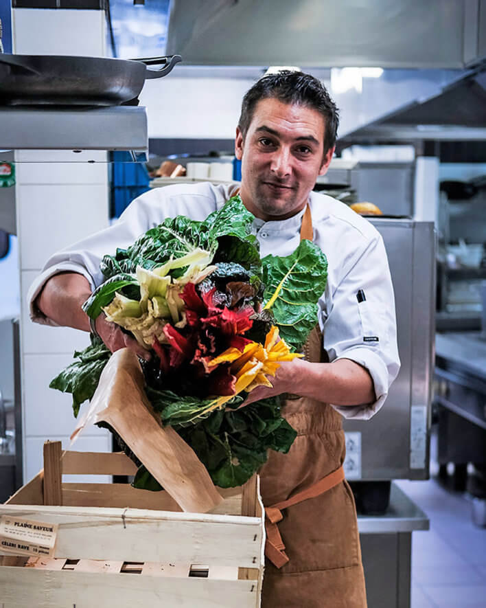 un chef en cuisine sort des légumes d'une cagette en bois