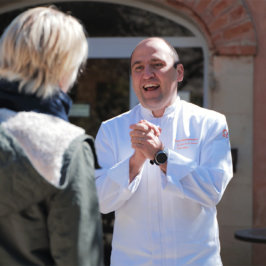 Un chef en veste blanche parle à une voyageusede dos