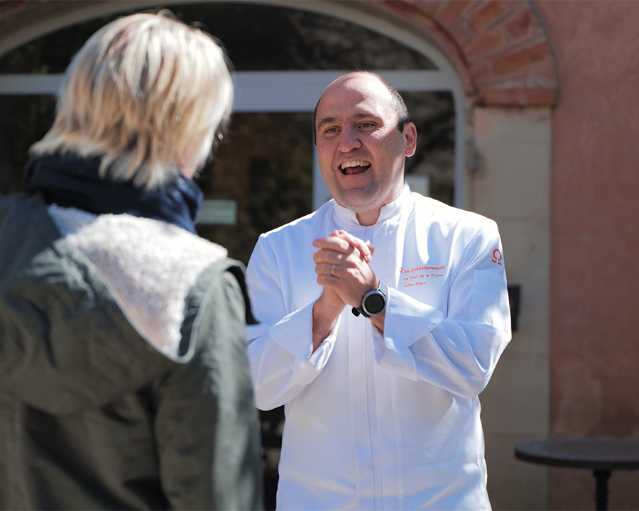 Un chef en veste blanche parle à une voyageusede dos